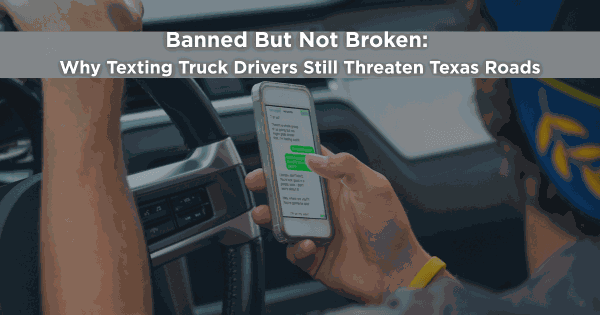 Truck driver holding a smartphone and texting while driving, illustrating the dangers of distracted commercial driving on Texas roads.